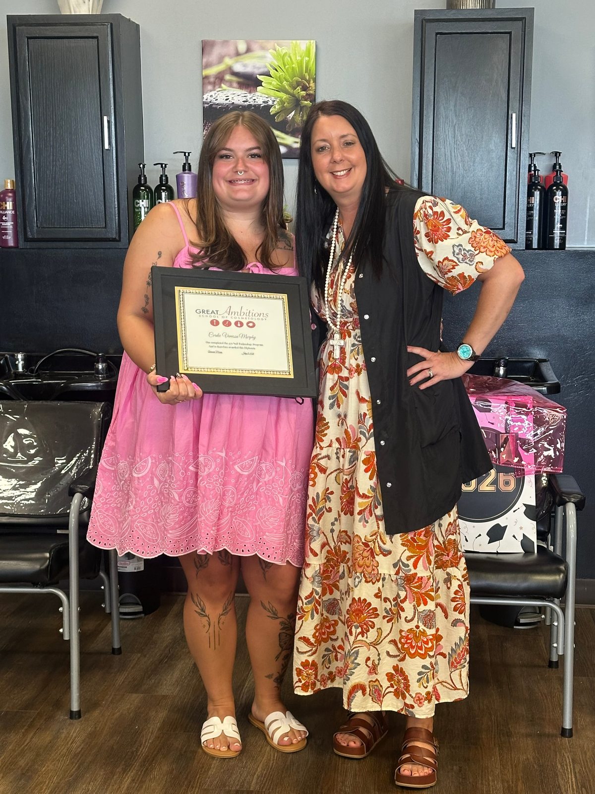 A Great Ambitions student celebrating her diploma with her instructor in the salon